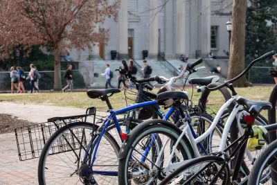 Close-up of crowded bike rack on university campus with students walking in background.