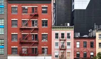 Three brick apartment buildings of various heights with fire escapes in New York City.