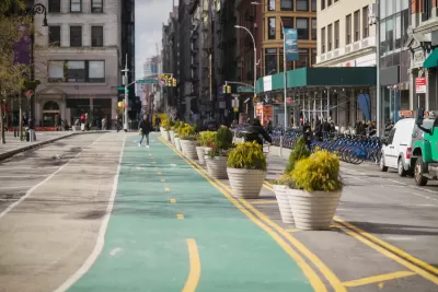 Green painted bike lane in New York City protected by concrete planters with Citi Bike station visible in background on sidewalk.