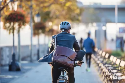 Rear view of man riding electric bike wearing business suit with large leather messenger bag slung across his back