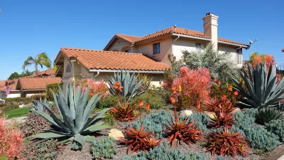 Drought tolerant desert plants including large agaves in the front yard of a Spanish-style Southern California home with red tile roof.