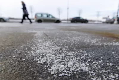 Low close-up of salt sprinkled on asphalt road in winter with person walking and car in background.