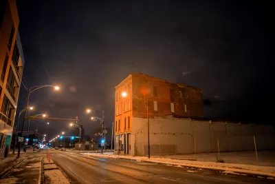 View of Chicago street with vacant lot and brick building, snow on the ground, at night.