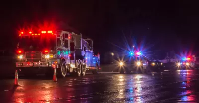 Nighttime view of fire truck and police cars with flashing lights on parked in a wet street