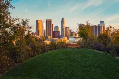 View of downtown Los Angeles at golden hour from top of grassy hill with wooden bench in Vista Hermosa Natural Park