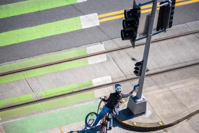 Cyclist pressing crossing button at green painted crosswalk.