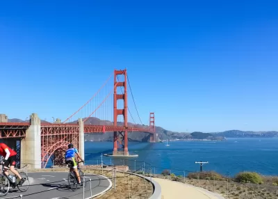 Two cyclists on a paved bike path overlooking the Golden Gate Bridge, San Francisco, California.