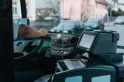 CLose-up of bus driver from behind with only hand on steering wheel visible.