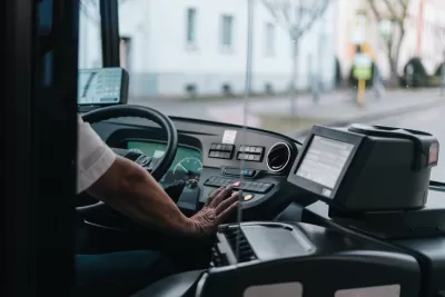 Close-up of bus driver from behind with only hand visible on steering wheel.