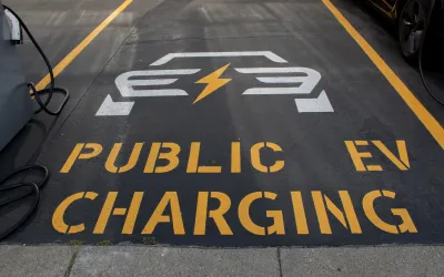 "Public EV Charging" sign with logo stenciled on black asphalt in parking lot.