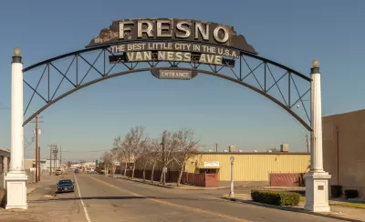 View of wide, deserted-looking street with arched sign reading "Fresno - Best little city in the U.S.A. - Van Ness Avenue - Entrance" in Fresno, California.