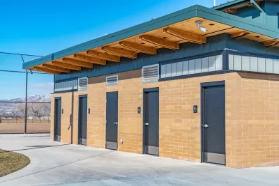 Row of four public restrooms outdoors with snowy mountain in background.