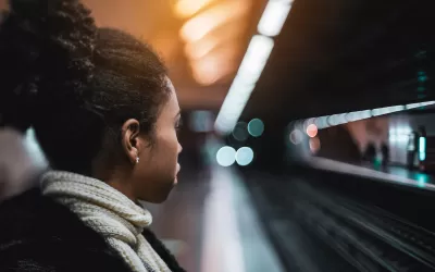 Close-up of woman waiting on fairly empty subway platform with tracks and opposing platform blurred in the background.