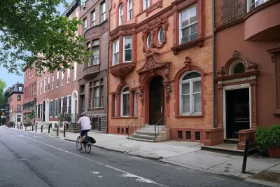 Person on bike rides in marked bike lane with brownstone homes in background in Phialdelphia, Pennsylvania.