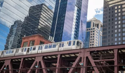 View up at Chicago elevated train line with train passing and glass high-rises in background.