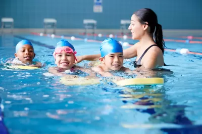 Female Coach In Water Giving Group Of Children Swimming Lesson In Indoor Pool.