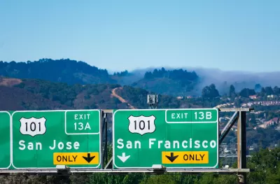 Close-up of green freeway signs pointing to US 101 to San Jose and San Francisco with foggy hills in background.