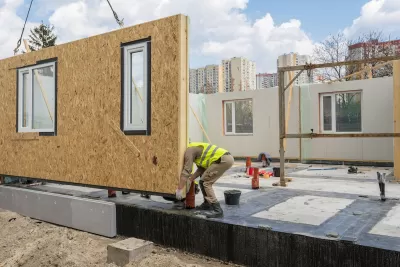 Worker in yellow construction vest working on modular home under construction.