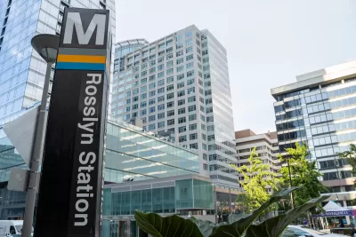 Close-up of Metro sign column at Rosslyn Station in Alexandria, Virginia with high-rose glass buildings in background.