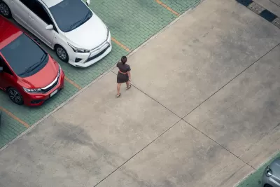 High view of woman walking in parking lot with red and white cars visible at left.