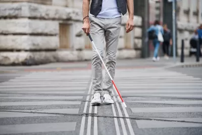 Low view of person with vision impairment cane walking through crosswalk.
