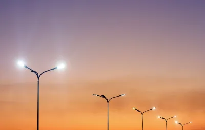 Row of double-headed street lights against orange sunset sky.