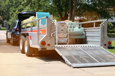 SUV with small open trailer hooked up filled with furniture for moving.