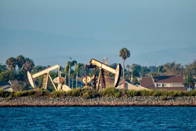 Oil drilling pumps on a wetland beach in California with houses in background