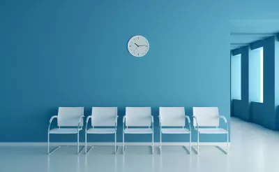 Row of five white chairs set against a blue wall with a round white analog clock. Clinic waiting room.