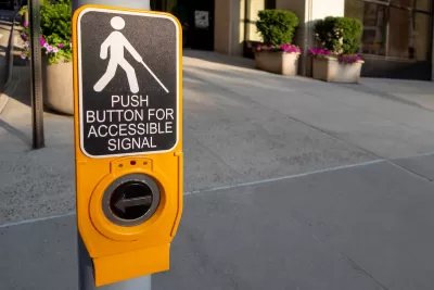 Close-up of yellow pedestrian crossing signal button with text "Push button for accessible signal" and diagram of person holding cane, indicating blindness.