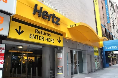 Yellow Hertz rental car log above sign "Returns ENTER HERE" and arrow above urban garage entrance.
