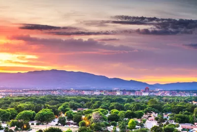 View of Albuquerque, New Mexico with green trees in foreground, mountains in background against sunset sky.