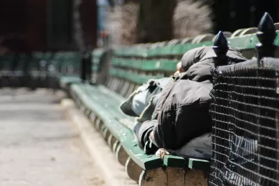 Person in black hoodie sleeping on green park bench in New York City park