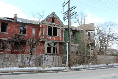 Vacant two-story red brick home in Detroit with missing windows.
