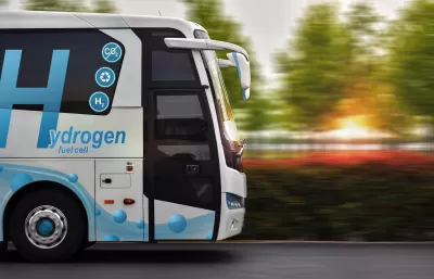 Side view of white bus with blue hydrogen fuel logo driving down the street.