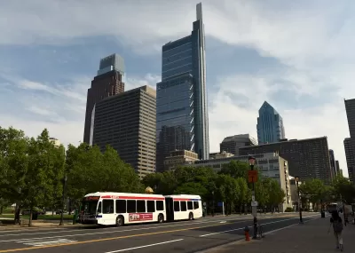 White city bus on road in Philadelphia, Pennsylvania with tall city buildings in background.