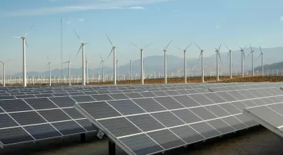 Large solar panel installation and wind turbines with Southern California desert mountains in background.