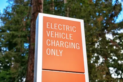 Orange sign with white "Electric vehicle charging only" sign outdoors with tree in background.