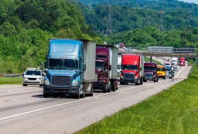 Line of multi-colored big rig trucks drivign down highway with other traffic including a yellow school bus.