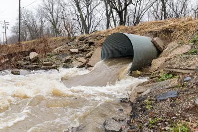 Large water pipe with brown water pouring out into dirt ditch.