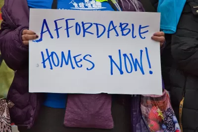 Close-up of person holding hand-written "Affordable Homes Now!" sign.