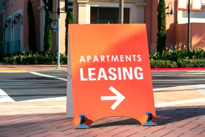 Orange "Apartments Leasing" sandwich board sign on sidewalk with arrow pointing right.