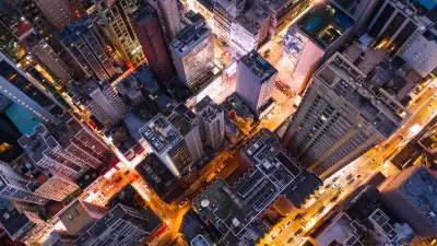 Bird's eye view of city skyscrapers at twilight with blurred lights on streets.