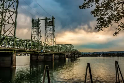 Green metal bridge over Columbia River between Oregon and Washington against cloudy sky.