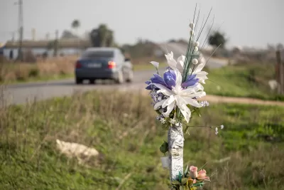 A bouquet of flowers stands in the grass beside a rural road as a car drives by.