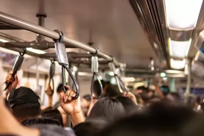 Close-up on passengers holding overhead straps on busy public transit bus.