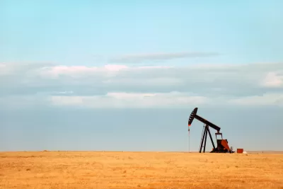 Single oil derrick on dry prairie with faded blue sky in background.