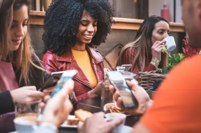 Close-up on group of young people sitting at a table using their cell phones.