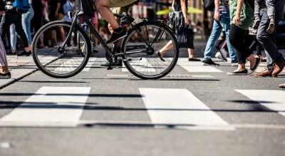 Low shot of pedestrians and a bike crossing a striped crosswalk.