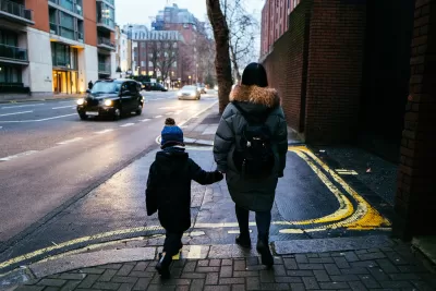 View from back of woman and child walking on London street wearing warm clothes with a black cab visible in background.